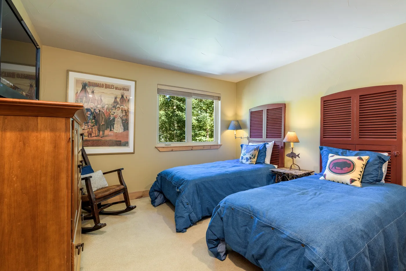Un dormitorio con dos camas vestidas con ropa azul y una ventana con vista a la vegetación.