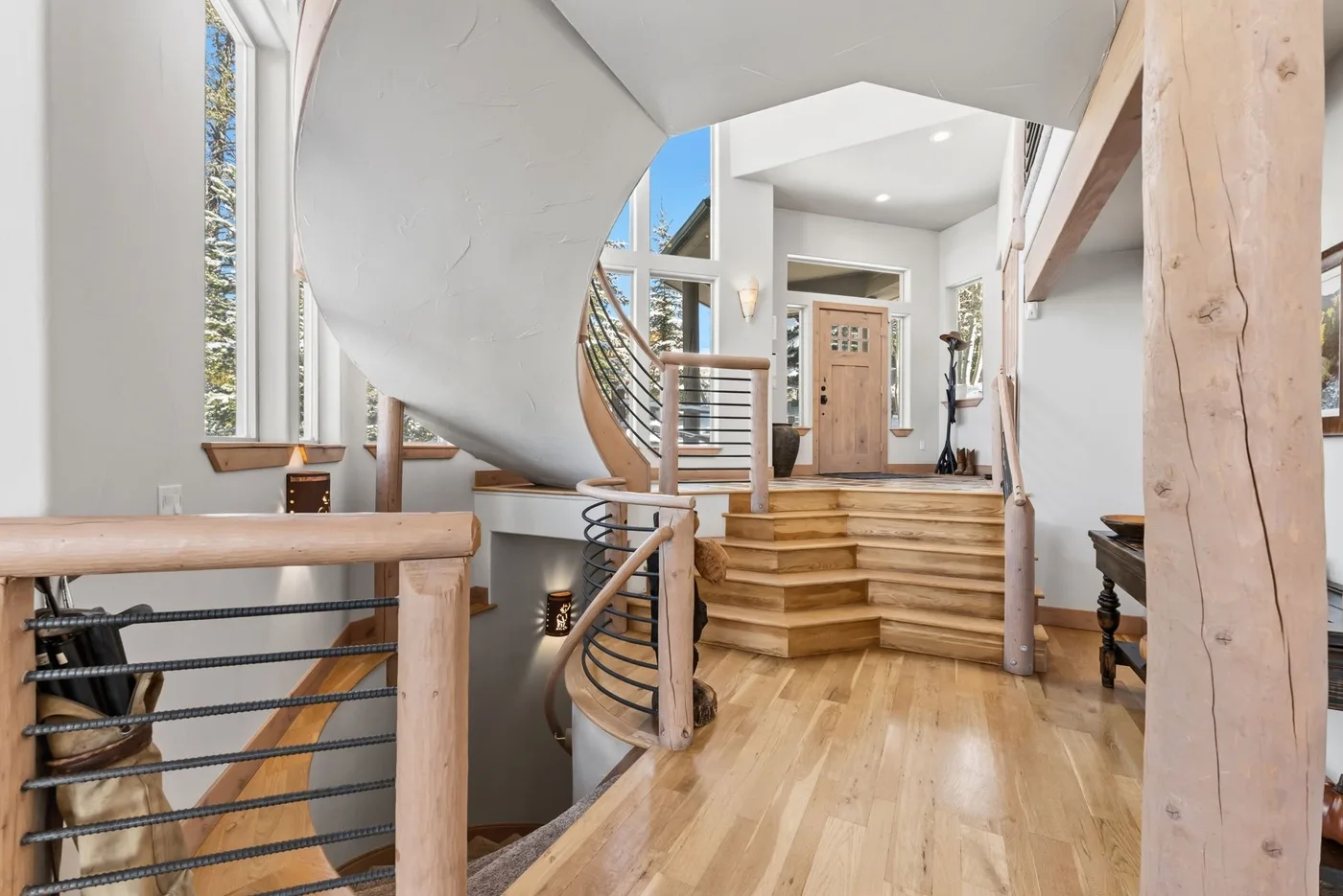Una entrada interior luminosa presenta una escalera curva y peldaños de madera.