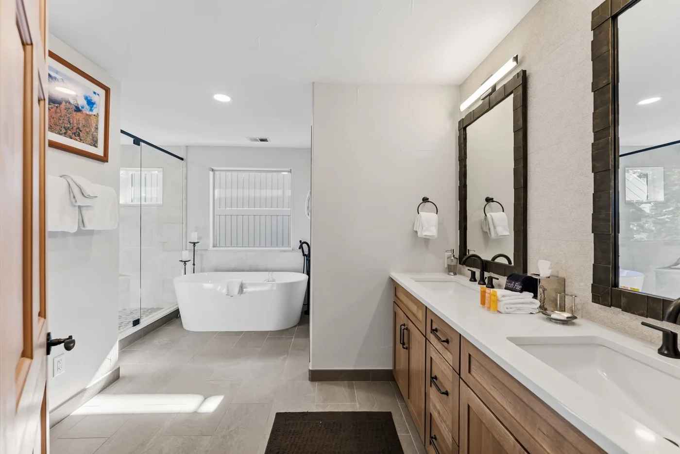 Un baño luminoso tiene bañera, ducha de vidrio y tocador con dos lavabos.