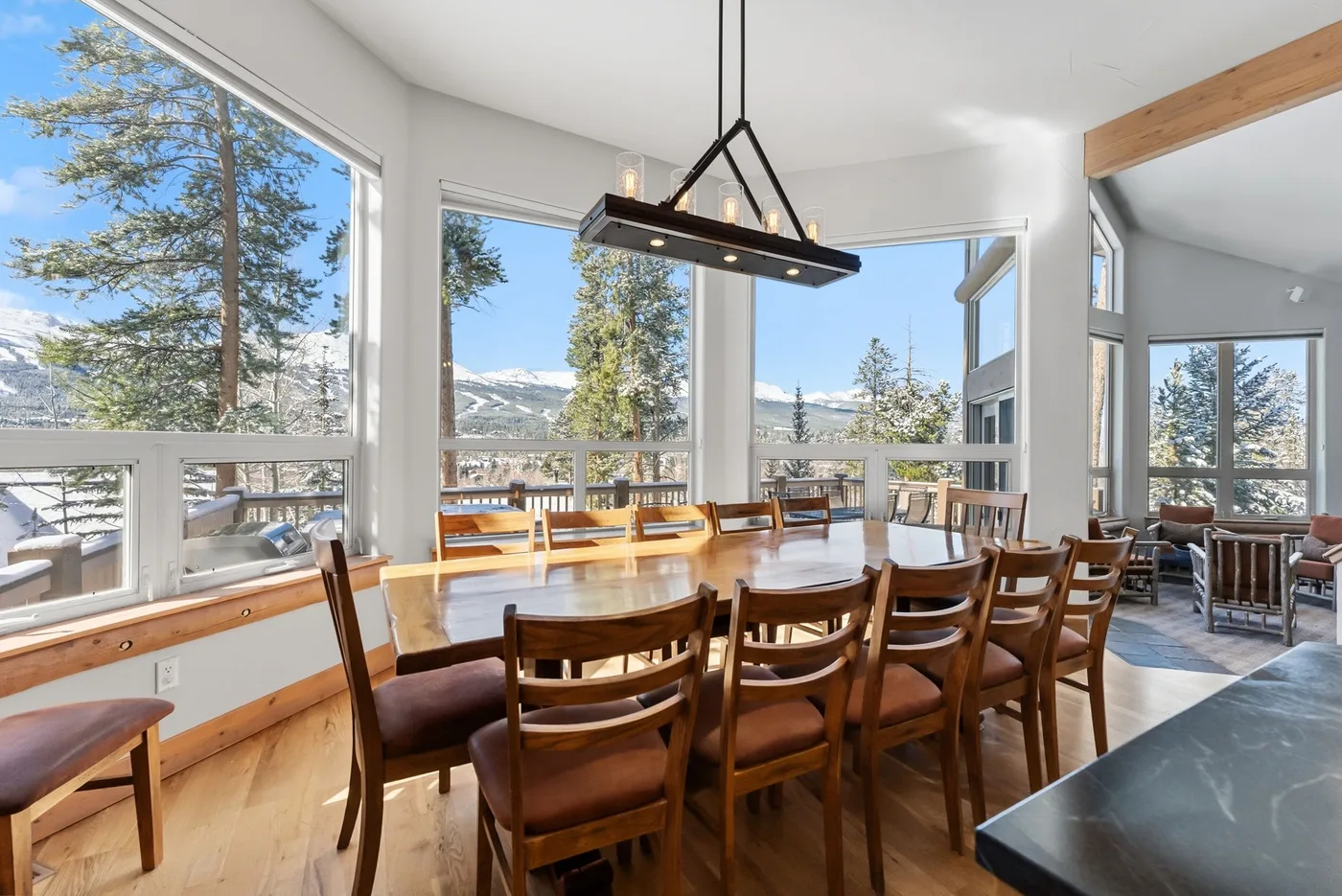 Comedor con una larga mesa de madera junto a grandes ventanales con vistas a un paisaje montañoso.