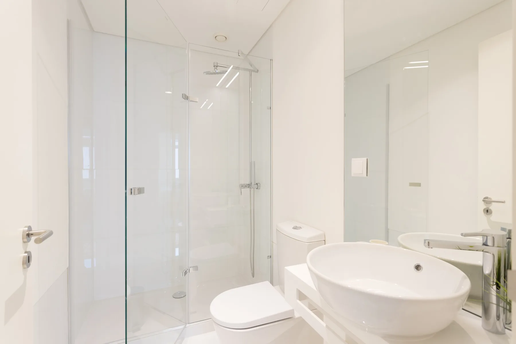 Un baño luminoso con ducha de vidrio, inodoro y lavabo ovalado.