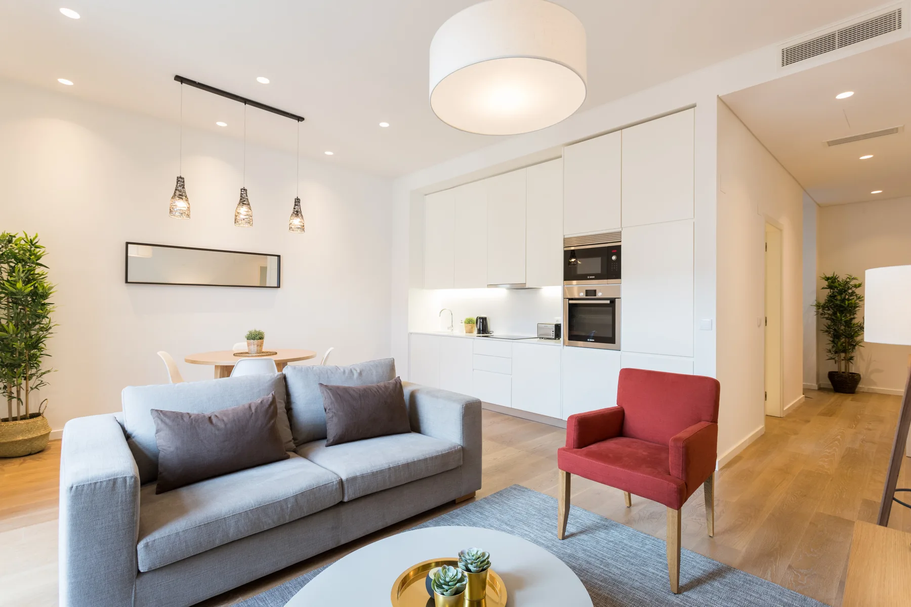Una sala luminosa con un sofá, un sillón y una cocina integrada.