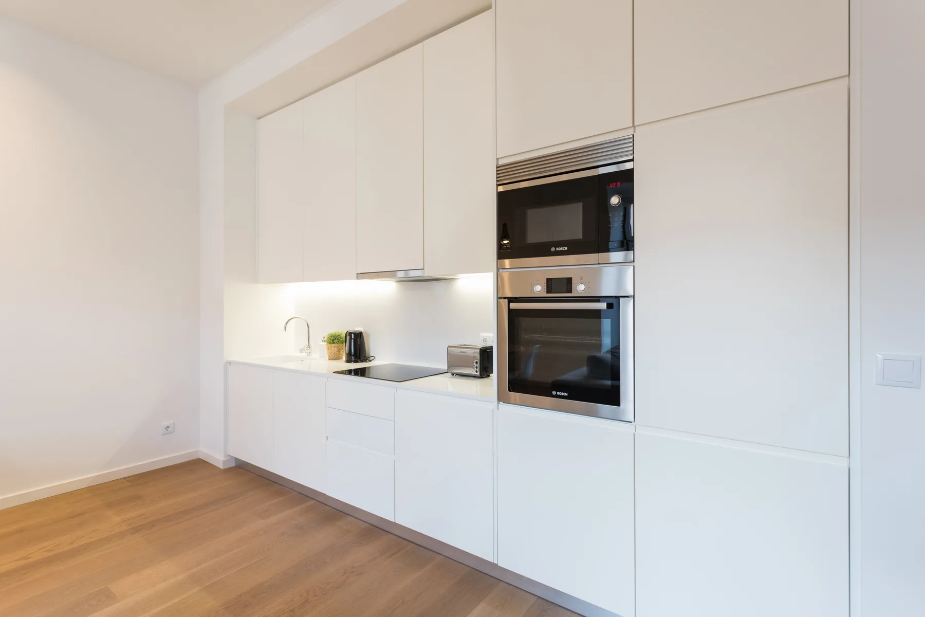 Una cocina luminosa y moderna con armarios blancos y electrodomésticos integrados.