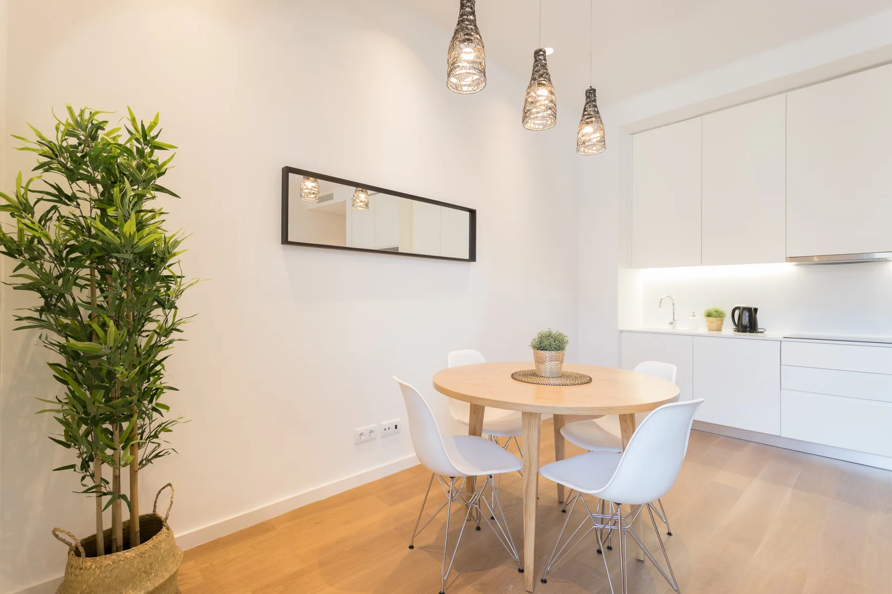 Comedor con una mesa redonda y asientos blancos junto a una cocina luminosa.