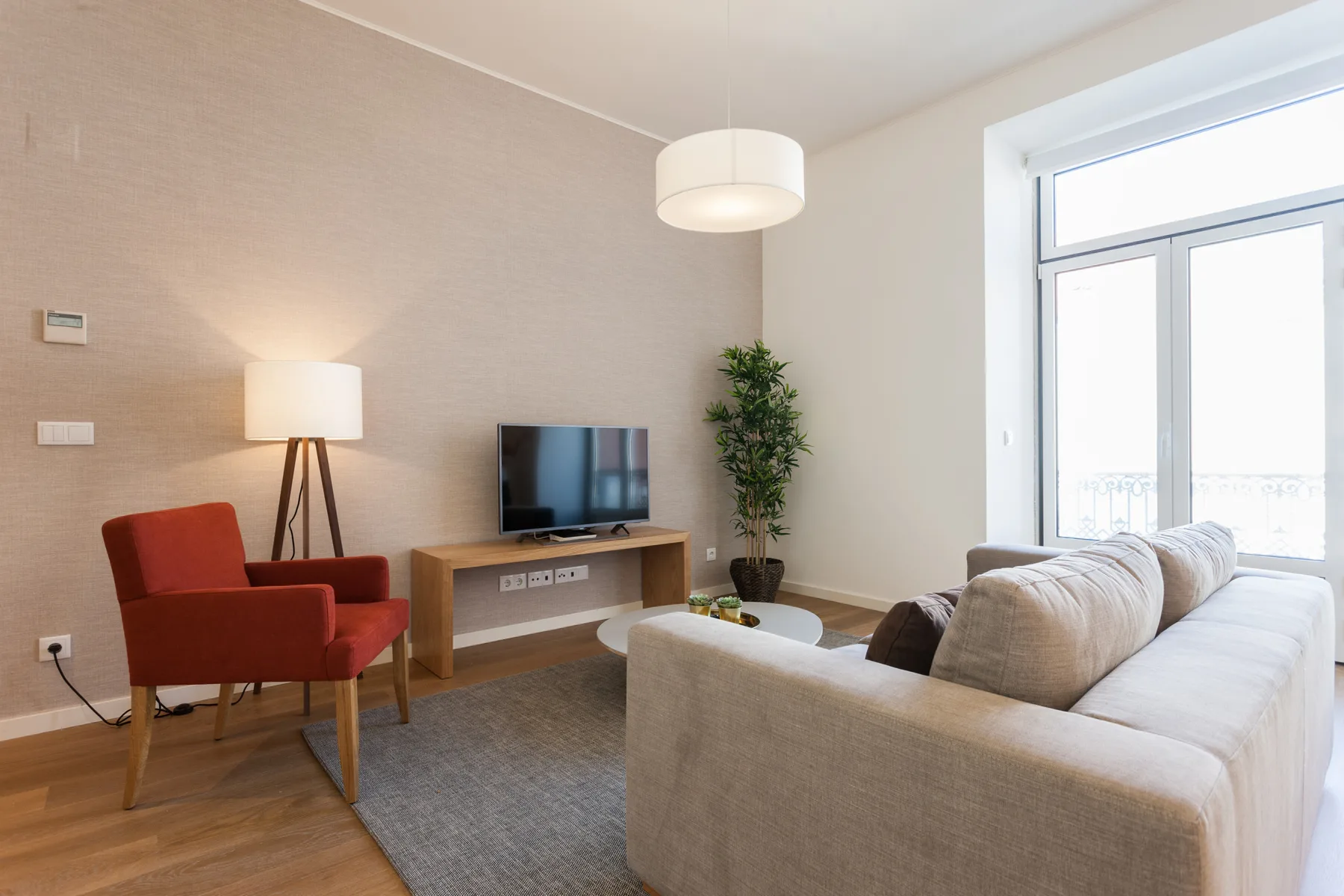Una sala luminosa con asientos, un televisor y grandes ventanas.