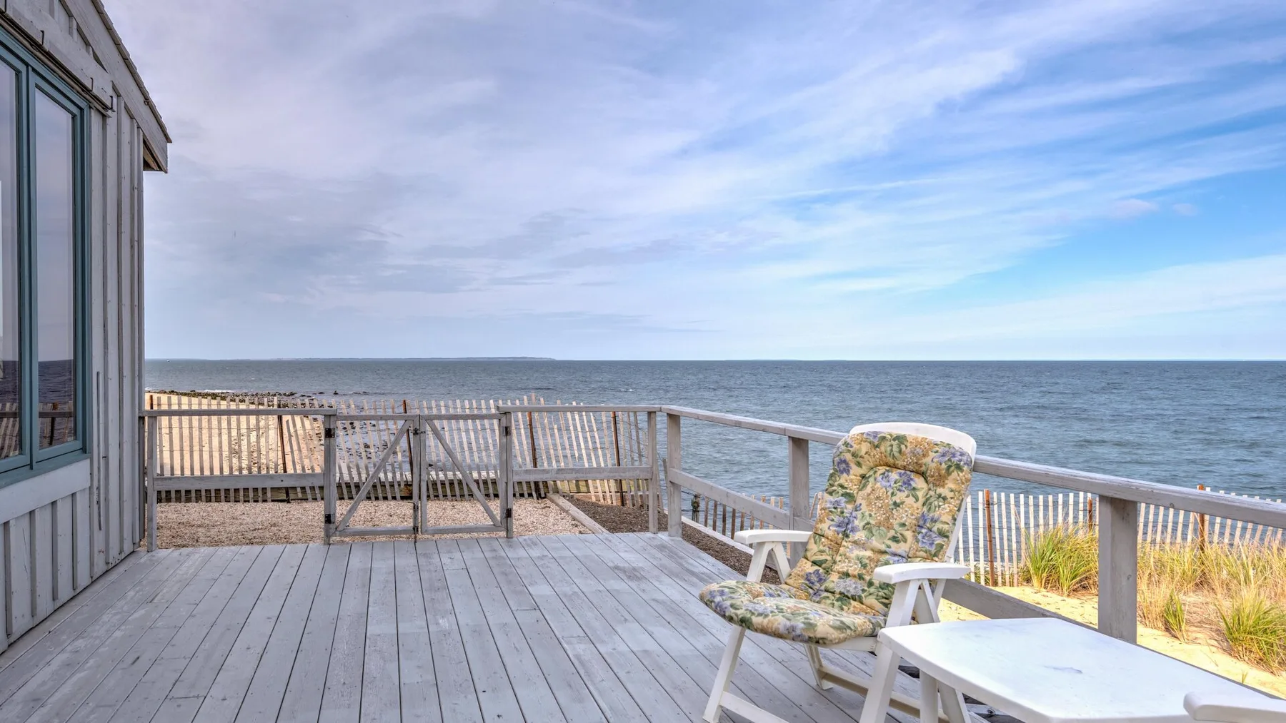 A wooden deck overlooks the ocean, with an outdoor chair near the railing.