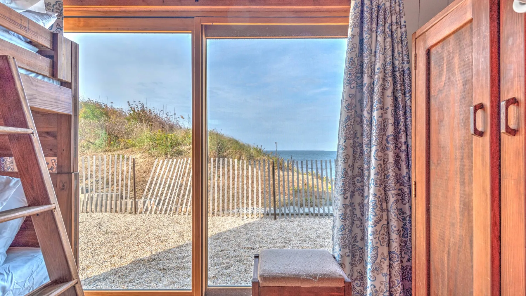 A bedroom with bunk beds beside a large window overlooking a sandy beach.