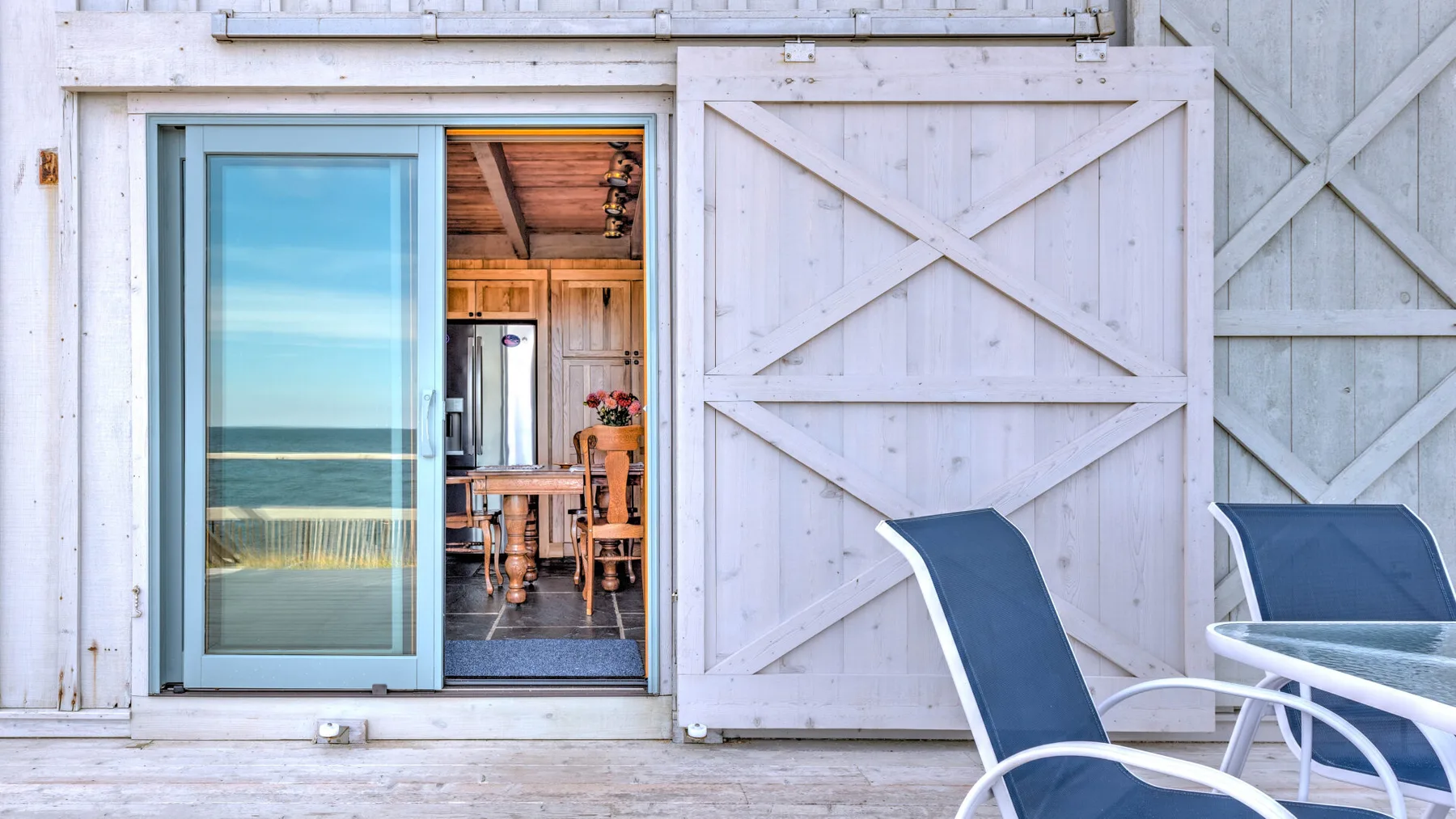 A white wooden patio with lounge seating beside an open sliding door.