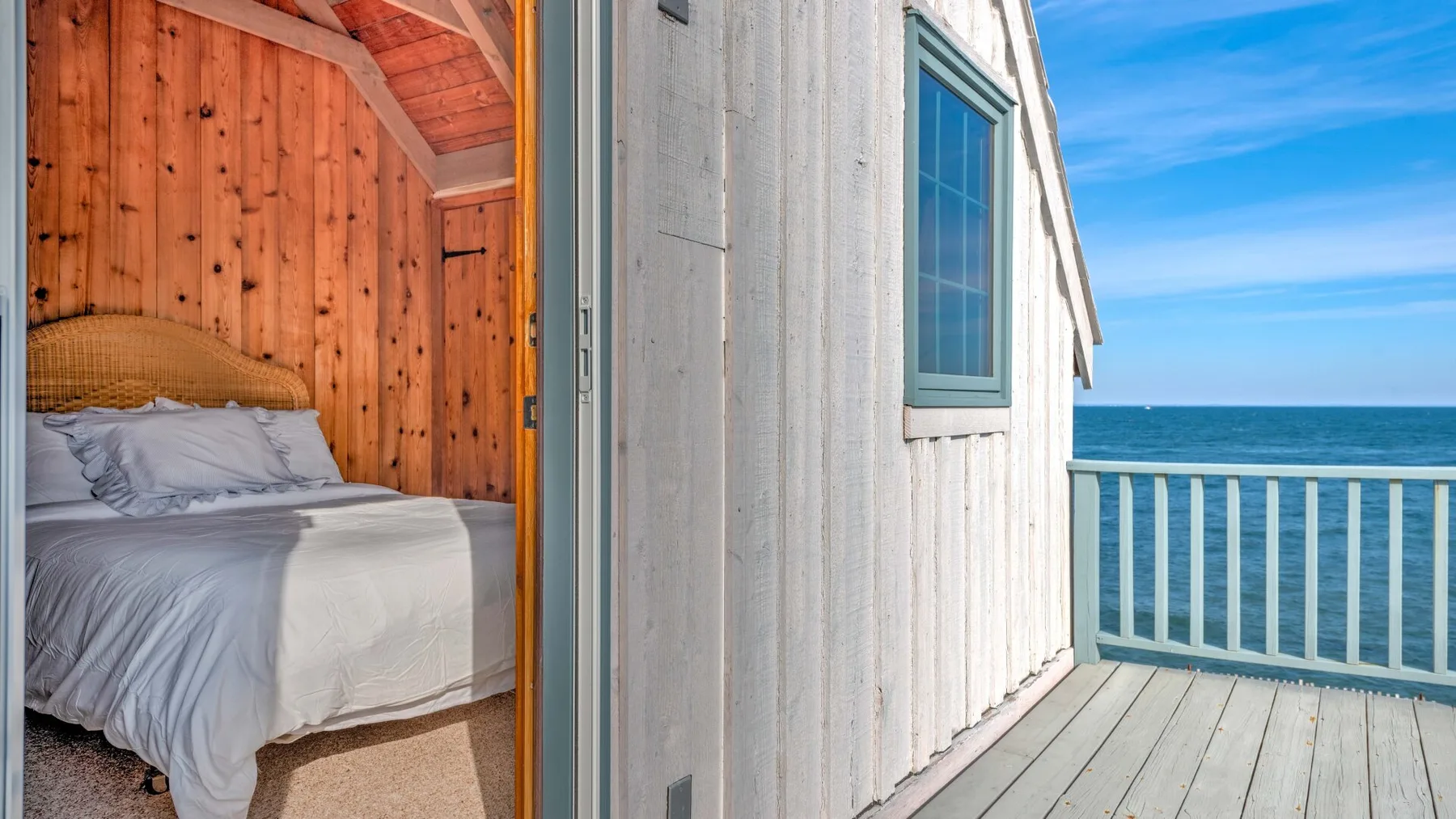 A bedroom with a bed opens onto a wooden deck overlooking the water.