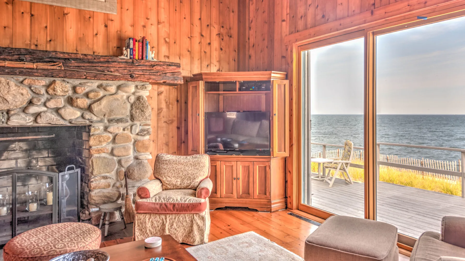A wood-paneled living room with a stone fireplace and seating beside sliding glass doors.