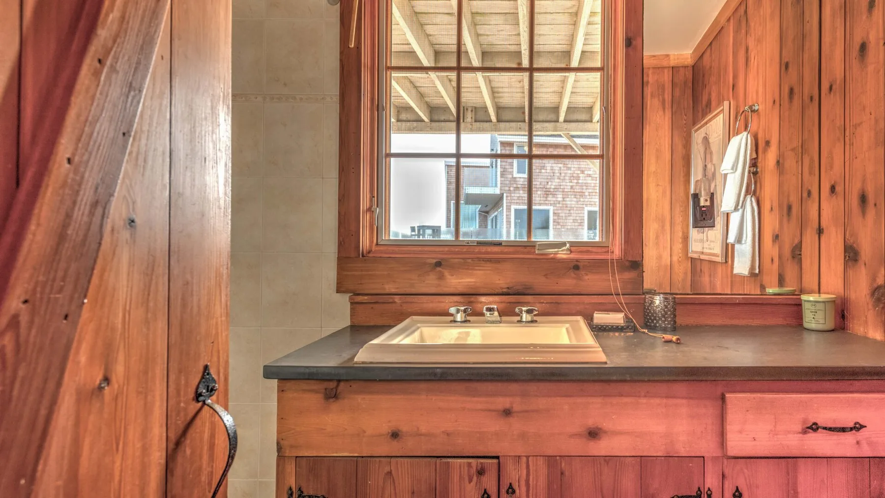 A wooden bathroom vanity with a sink sits beneath a large window.