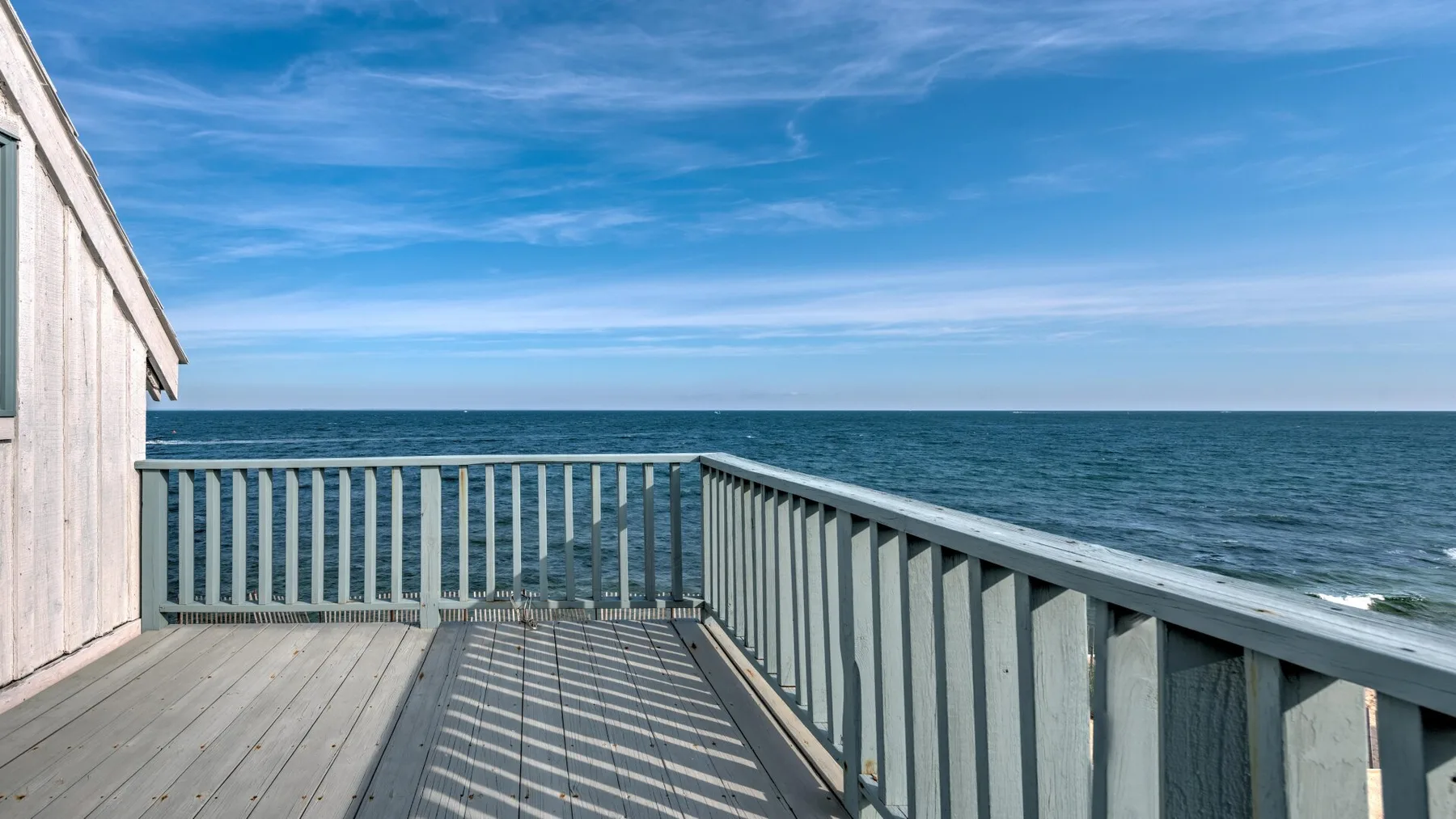 A wooden deck with railings overlooks the ocean beneath a blue sky.