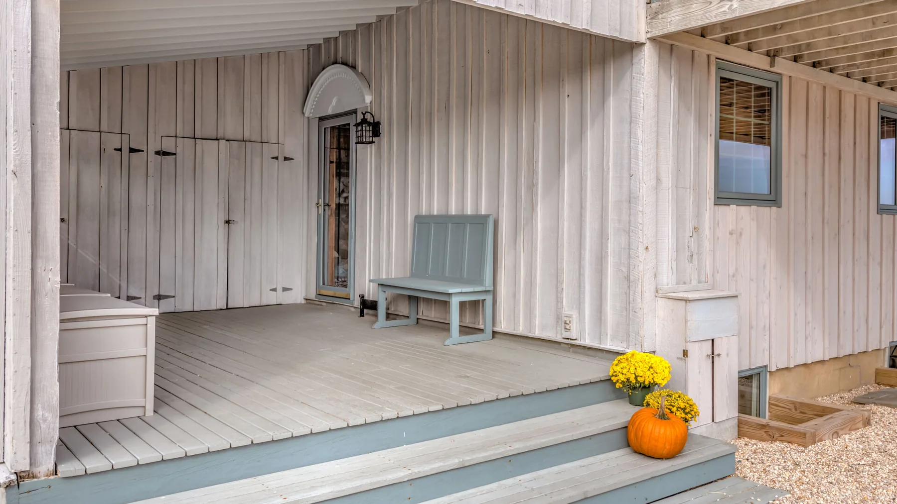 A covered porch with a bench and potted flowers beside the entrance.