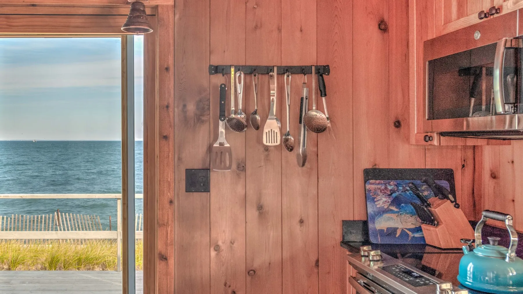 A wood-paneled kitchen with hanging utensils and a view of the sea through the window.