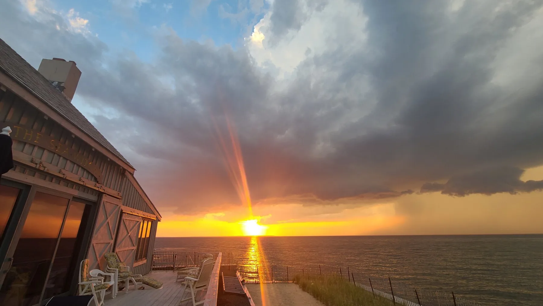 A waterfront deck beside a building overlooks the ocean at sunset.