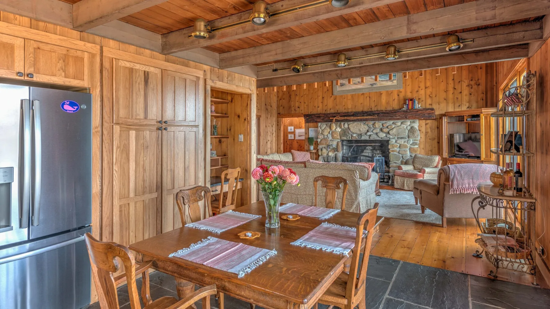 A wood-paneled living and dining room with a table and seating around a stone fireplace.