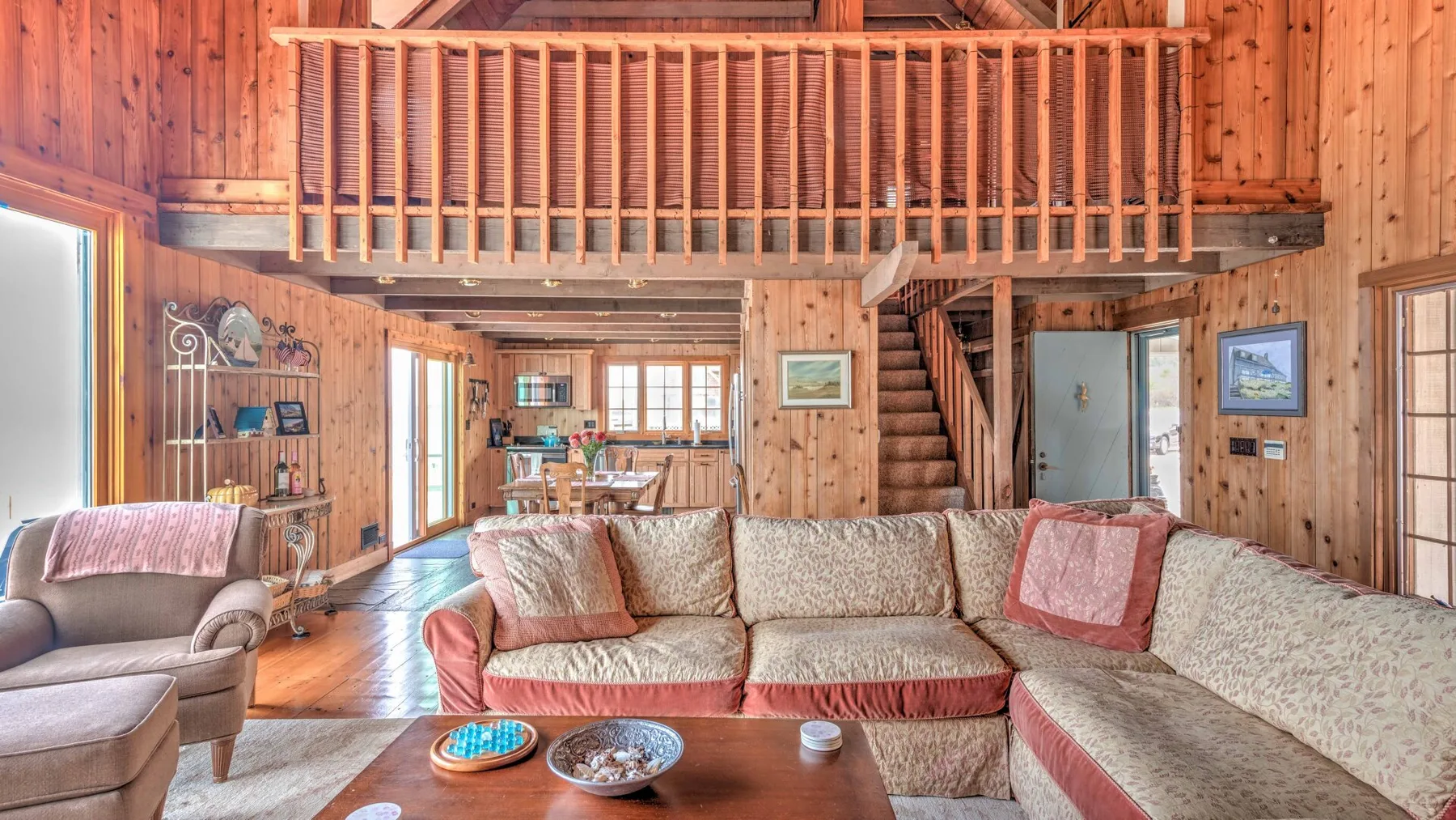 A wood-paneled living room with seating, a coffee table, and an upper-level railing.