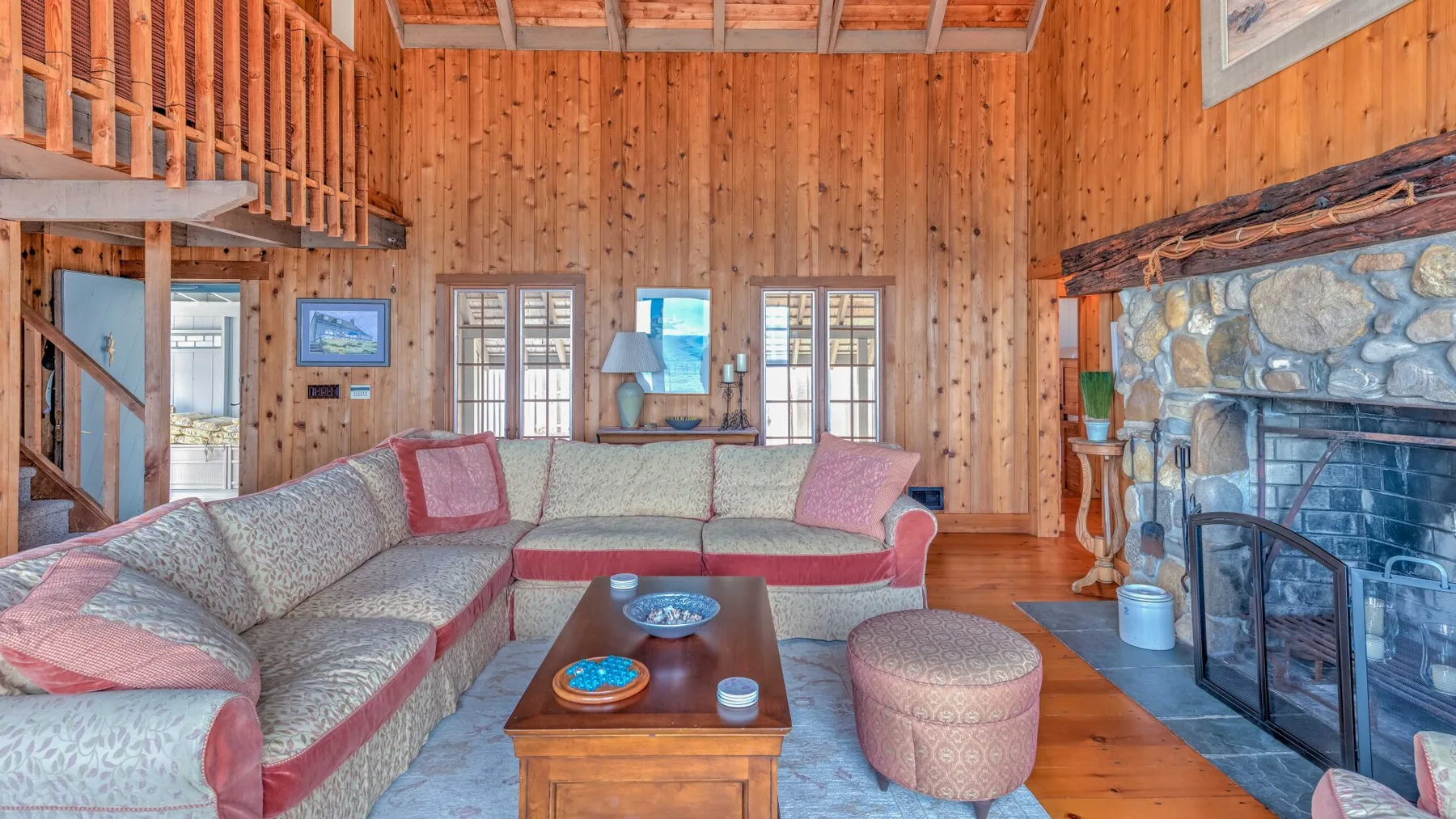 A wood-paneled living room with sectional seating and a stone fireplace.