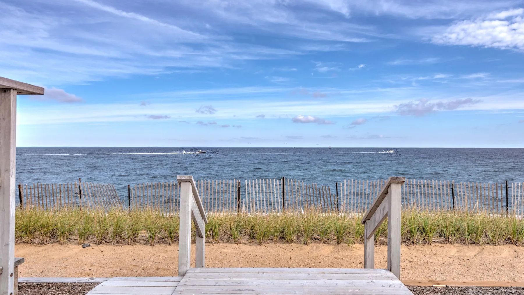 A sandy beach access path leads toward the ocean, bordered by dune grass and fencing.