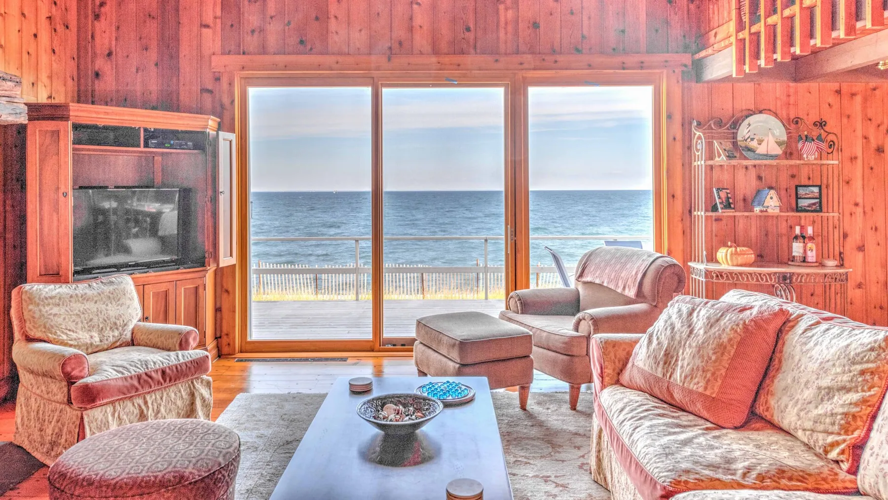 A wood-paneled living room opens onto a view of the ocean through large windows.
