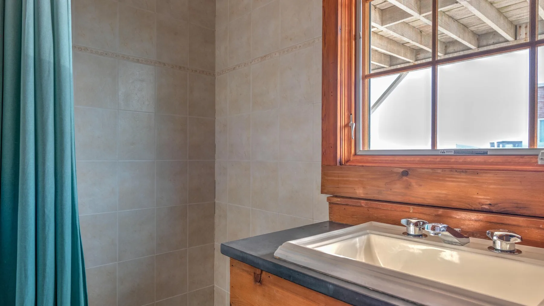 A tiled bathroom with a sink beneath a wood-framed window.