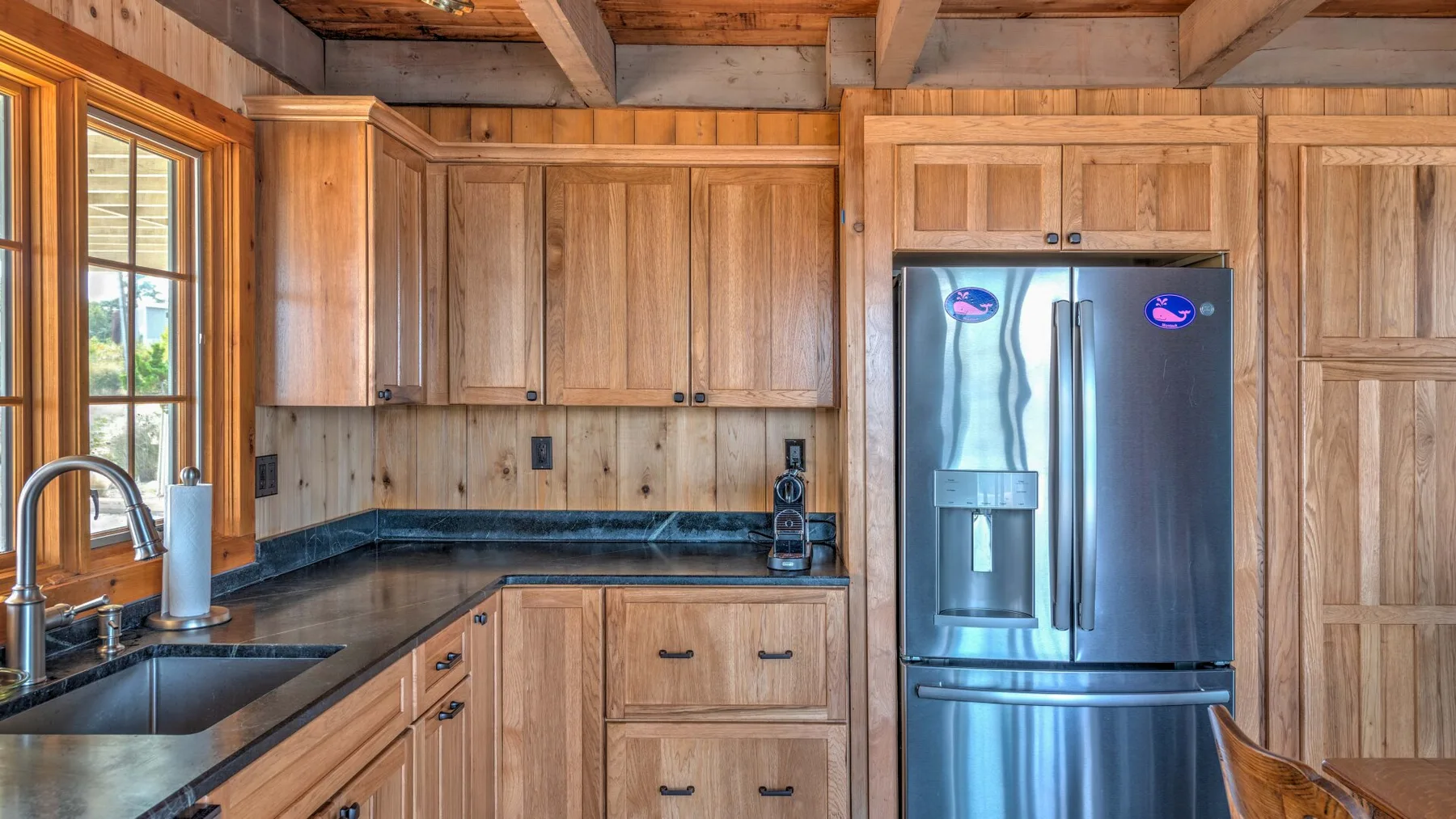 A wood-paneled kitchen with dark counters and a stainless steel refrigerator.