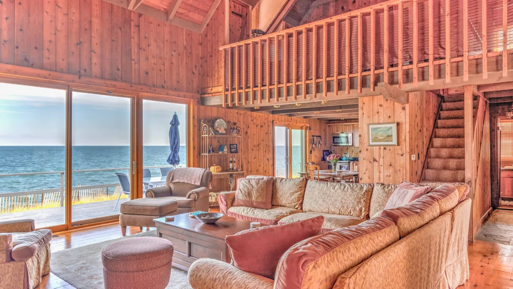 A wood-paneled living room with seating and large windows overlooking the water.