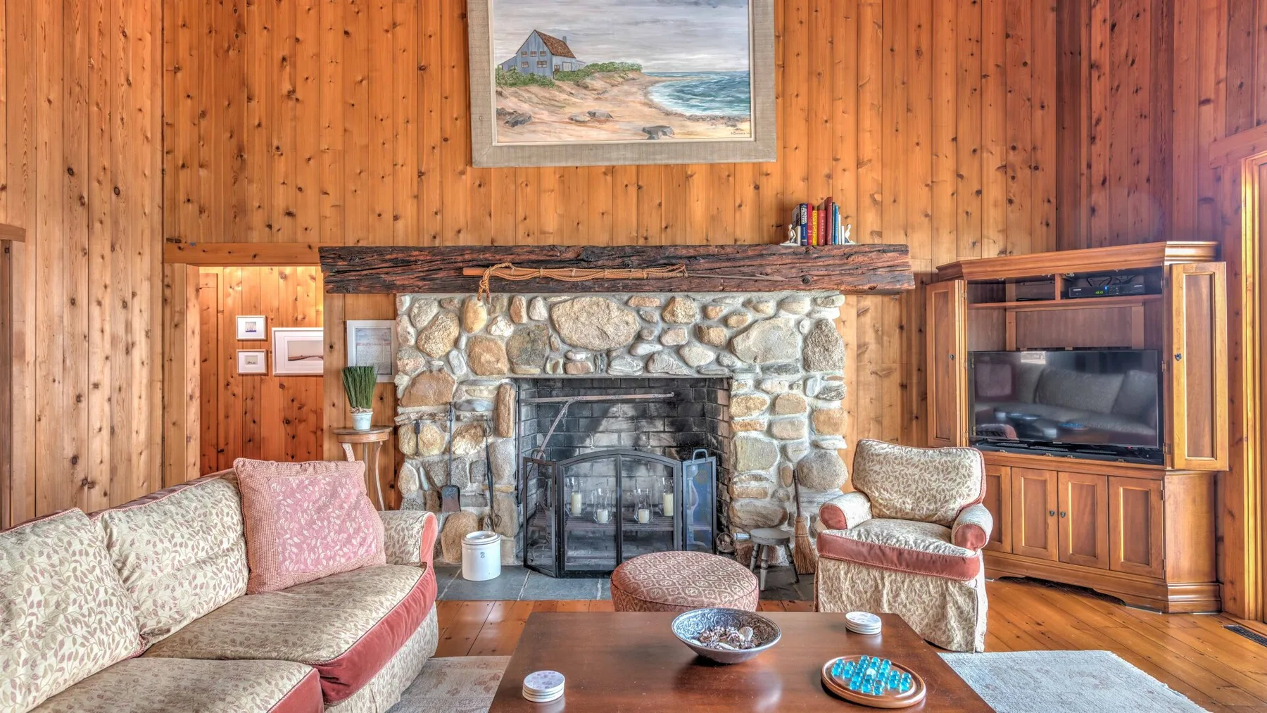 A wood-paneled living room centers on a stone fireplace, with seating and a television.