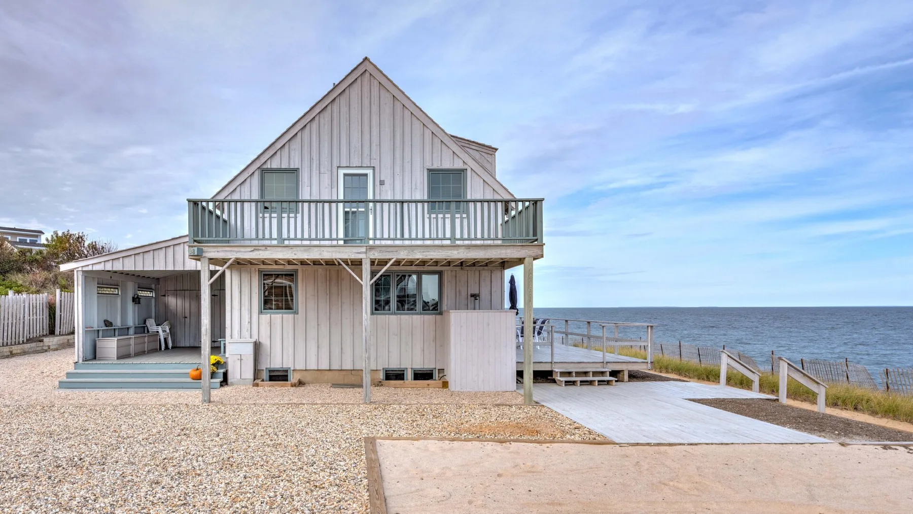 A raised coastal house with a balcony and a sloped path beside the water.