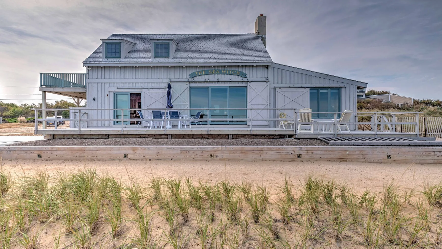 A beachside house with a raised deck and sandy dunes in front.