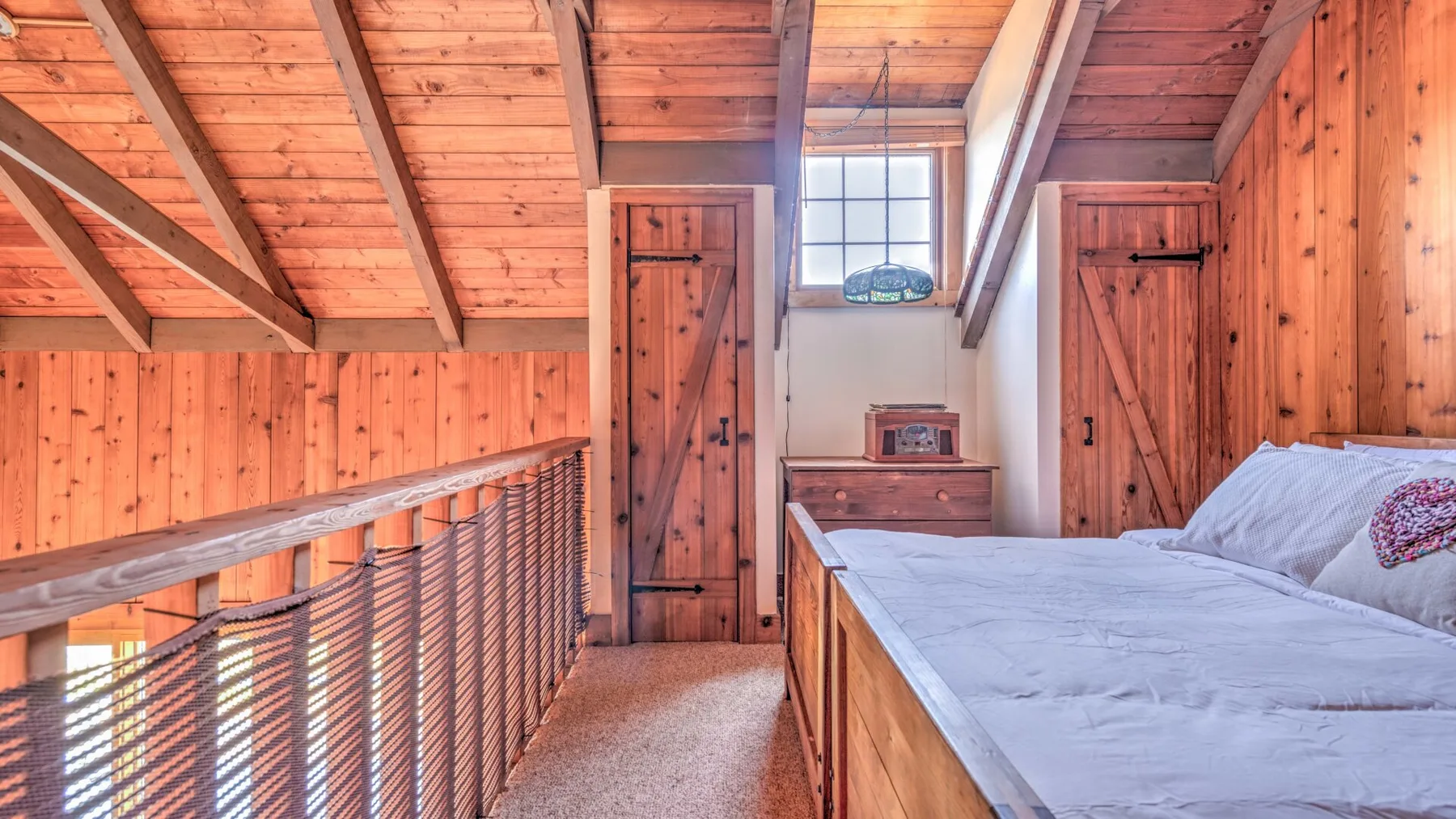 A wood-paneled loft bedroom with a bed beside a rope-railed stair opening.