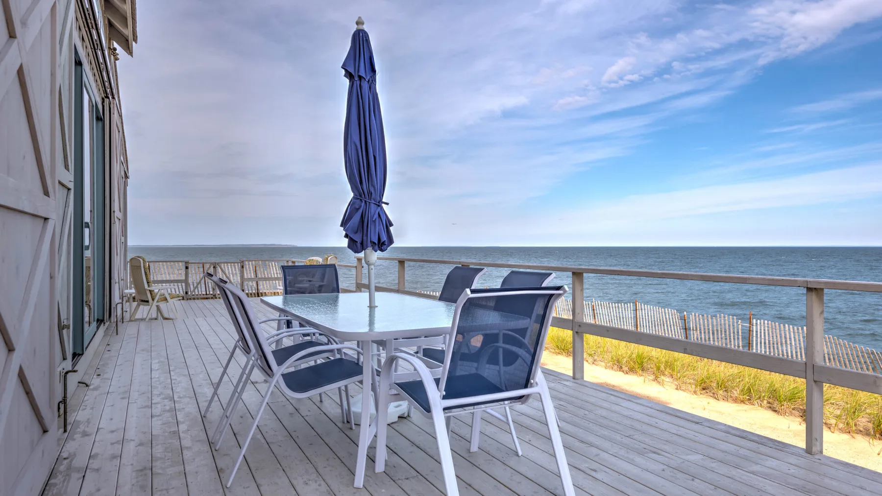A seaside deck has outdoor seating, a table, and a closed umbrella.