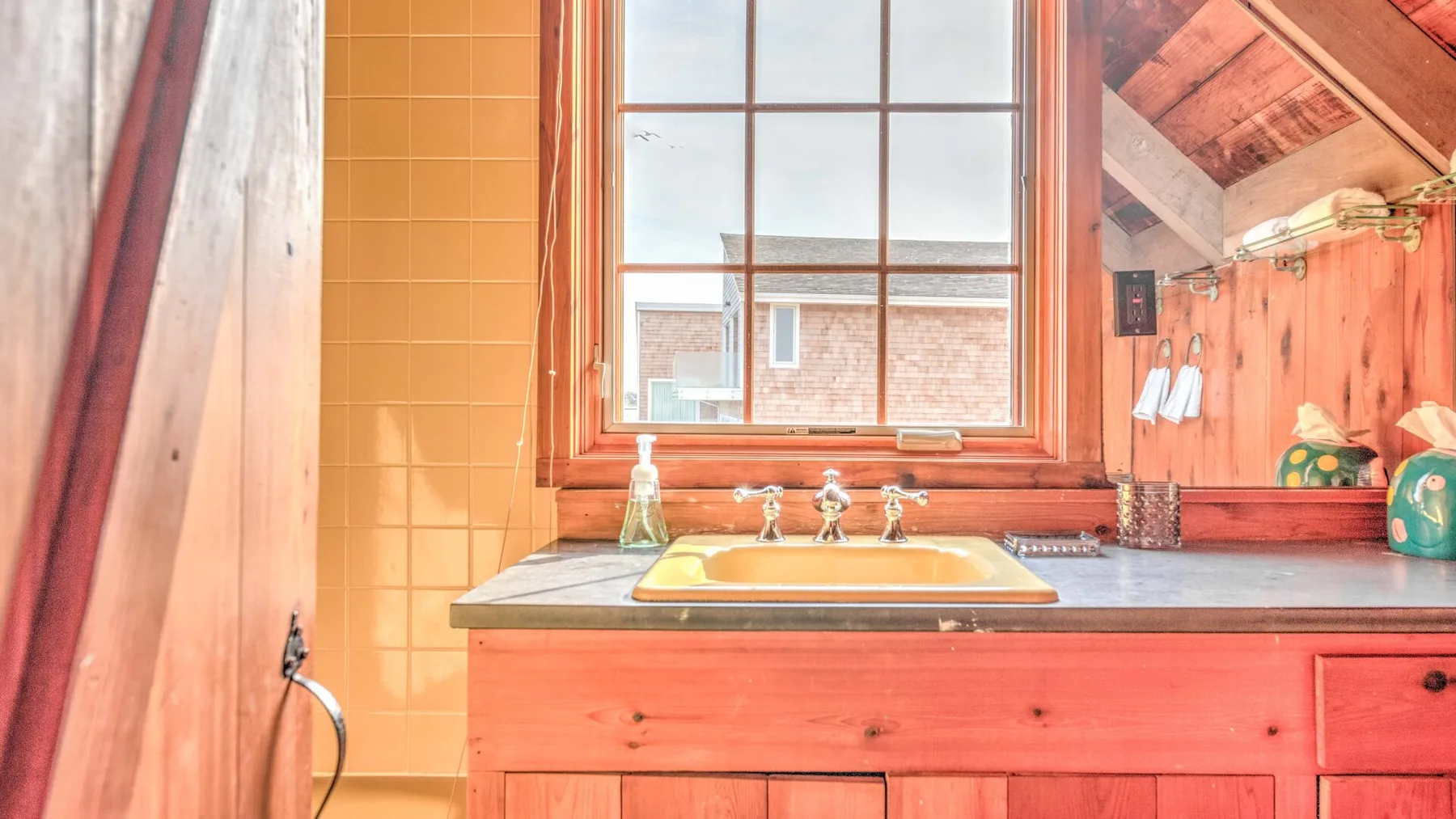 A bathroom vanity with a sink sits beneath a window beside a tiled shower area.
