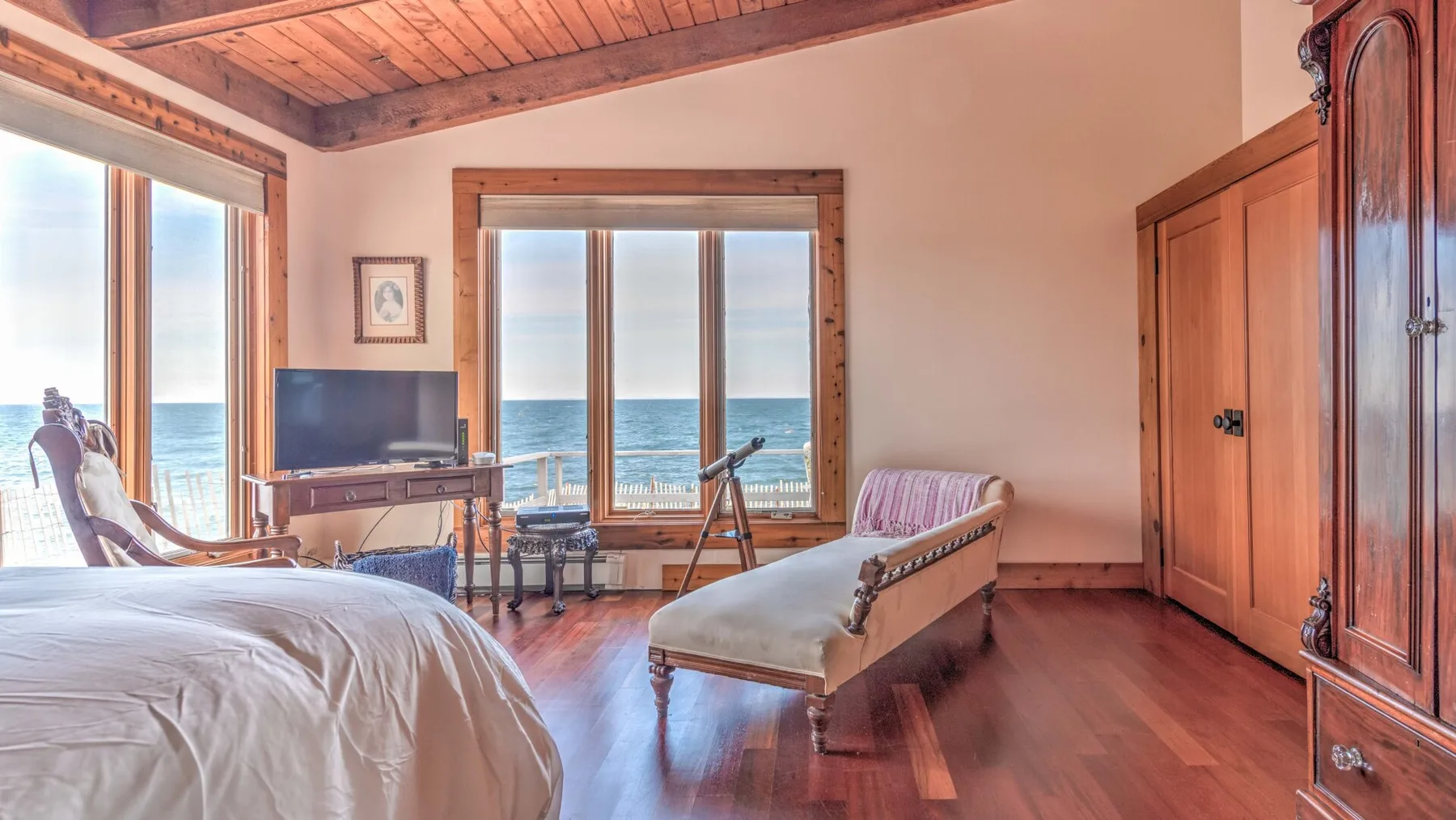 A bedroom with a bed, seating, and large windows overlooking the ocean.