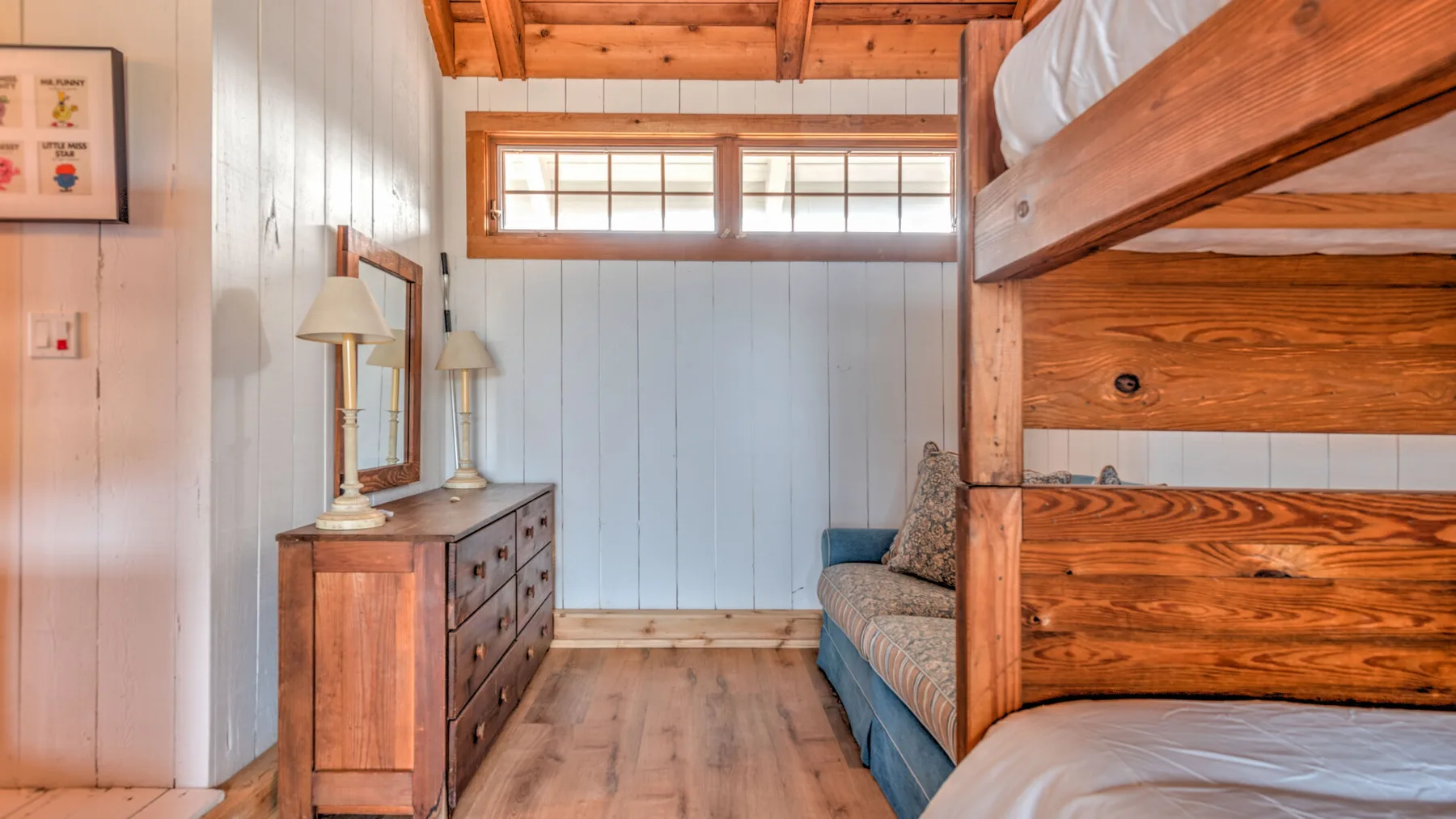 A bedroom with a wooden bunk bed, dresser, and narrow high windows.