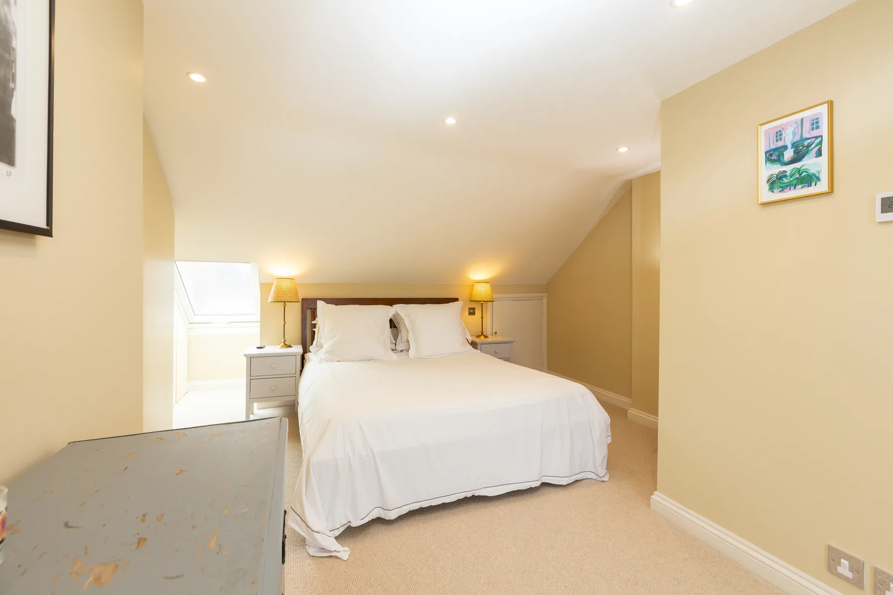 A bright bedroom with a neatly made bed beneath a sloped ceiling.