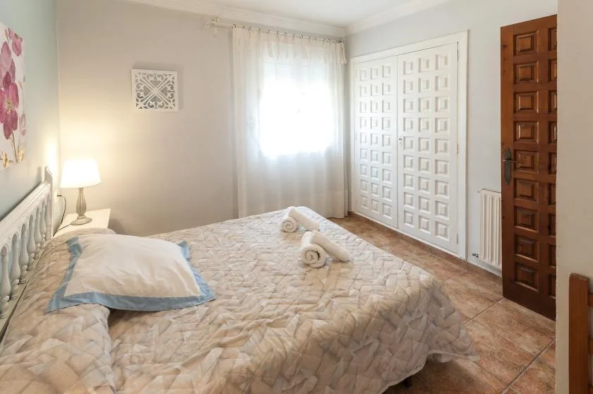 Un dormitorio con una cama, ropa de cama estampada, una ventana con cortina y puertas con paneles.