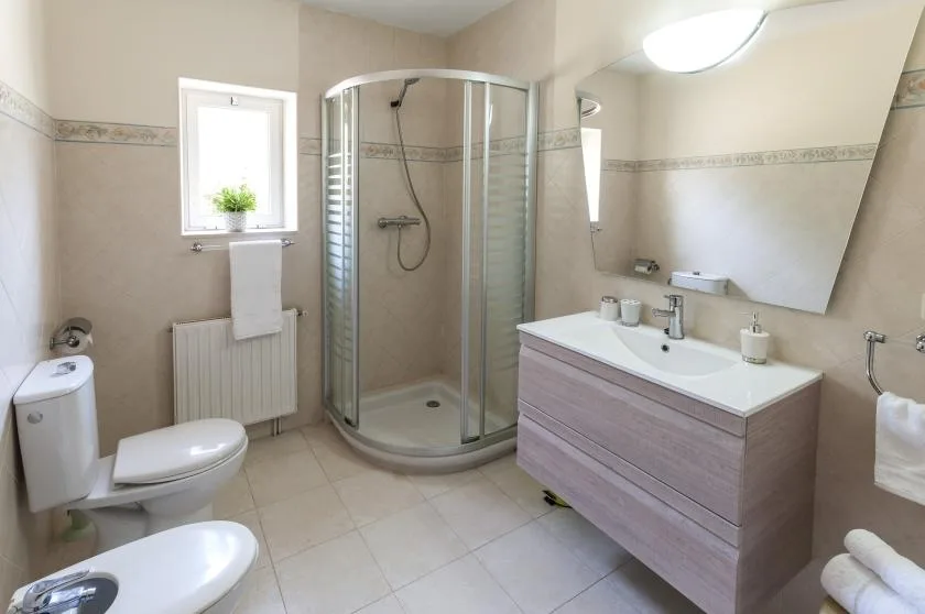 Un baño con azulejos, una ducha de vidrio curvada y un lavabo con mueble.