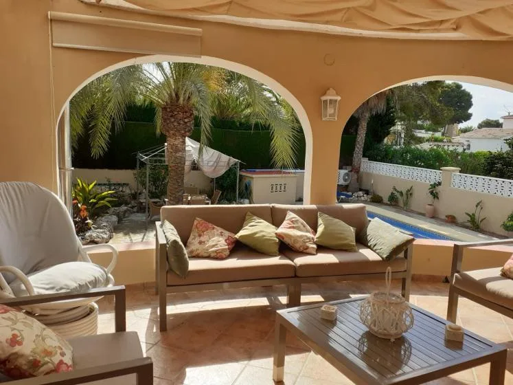 Una zona de estar en un patio sombreado da a un jardín y una piscina.