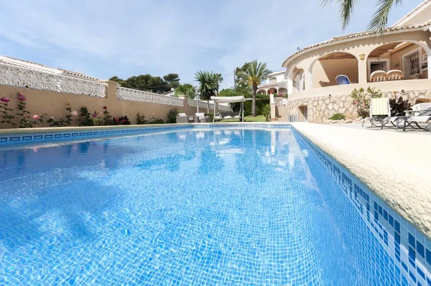 Una piscina junto a una villa, con asientos al borde alicatado.