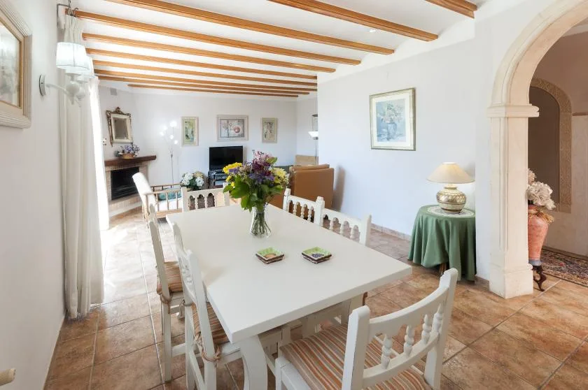 Un comedor luminoso con una mesa larga, sillas blancas y vigas expuestas en el techo.