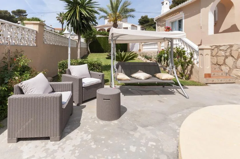 Un patio exterior pavimentado con asientos acolchados y un columpio de jardín cubierto.