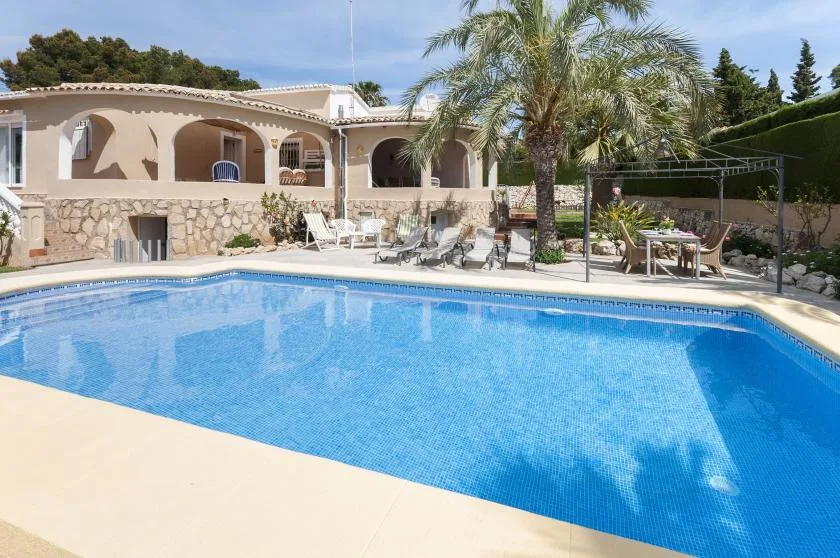 Una piscina al aire libre está junto a un patio ajardinado y una casa.