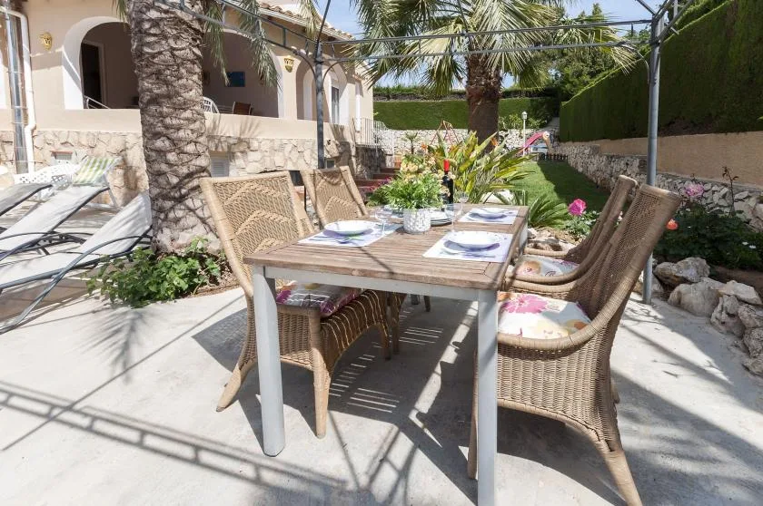 Comedor al aire libre con una mesa puesta y asientos de mimbre junto a una casa.