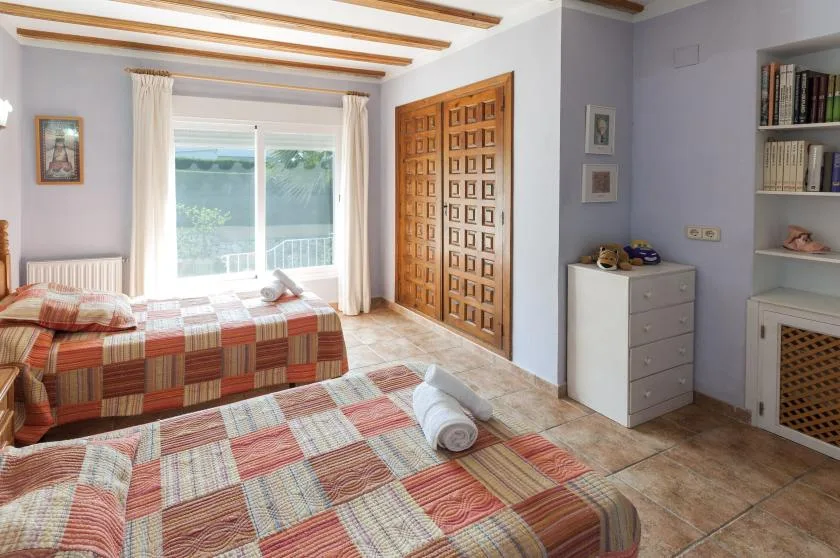 Un dormitorio con camas estampadas, una ventana grande y puertas de madera.