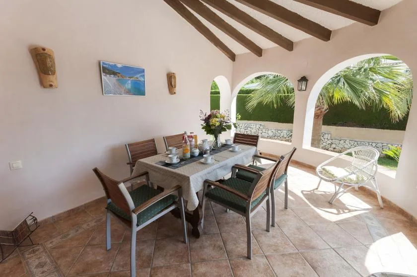 Comedor en un patio cubierto, con una mesa y arcos que dan a la vegetación.