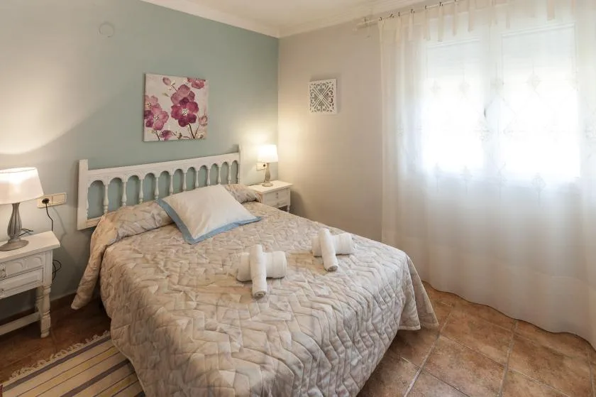 Un dormitorio con una cama doble, mesitas de noche y una ventana luminosa con cortinas.