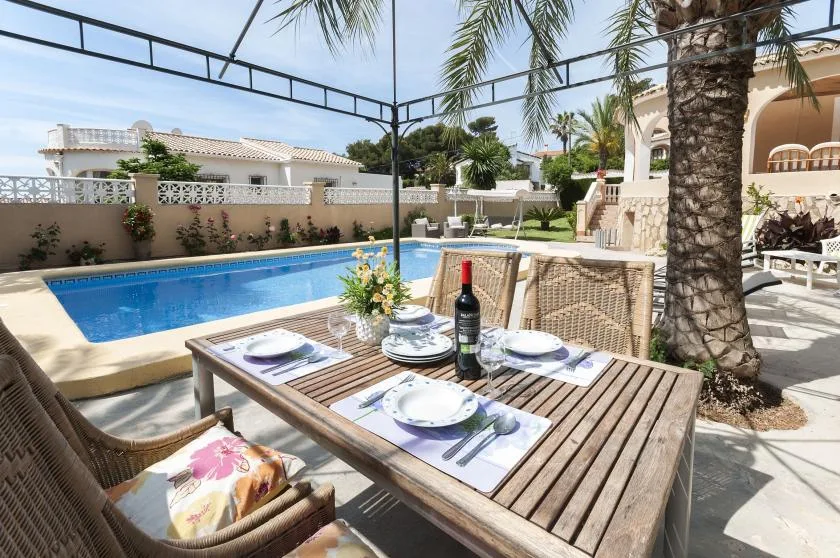 Zona de comedor al aire libre junto a una piscina, bajo una cubierta.