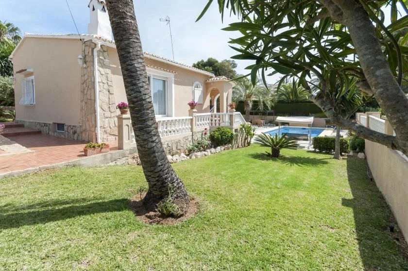 Una casa da a un césped verde, con una piscina visible al fondo.