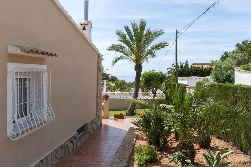 Exterior de una casa junto a un sendero de baldosas y un jardín con palmeras.